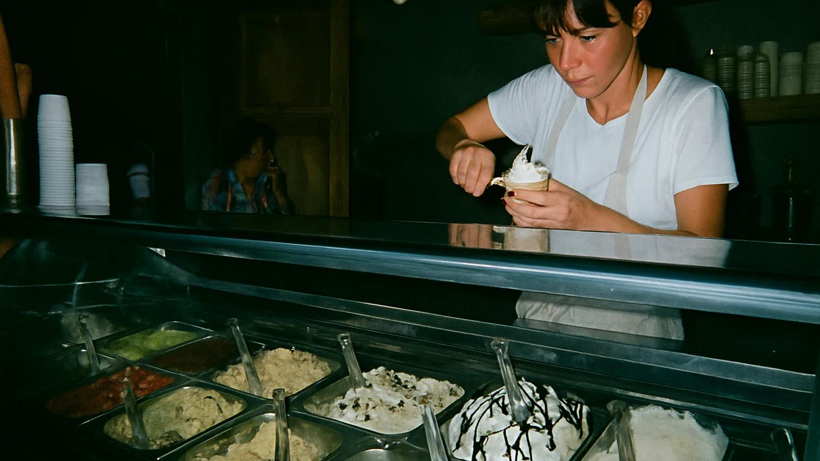 Staff member scooping ice cream behind the counter of a small parlour